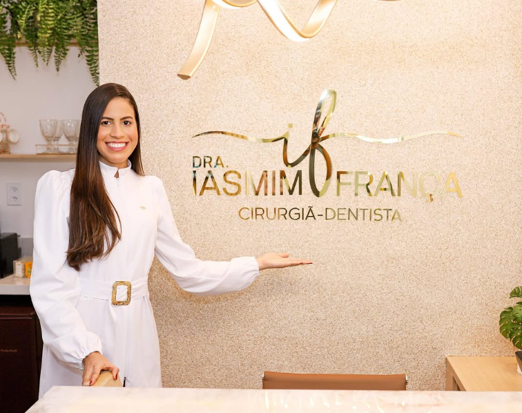 Dra. Iasmim França na recepção do consultório, ao lado de sua marca dourada
